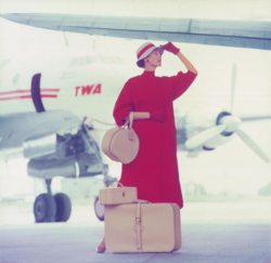 Femme vêtue de rouge avec des bagages aériens davant un avion de la compagnie américaine TWA,