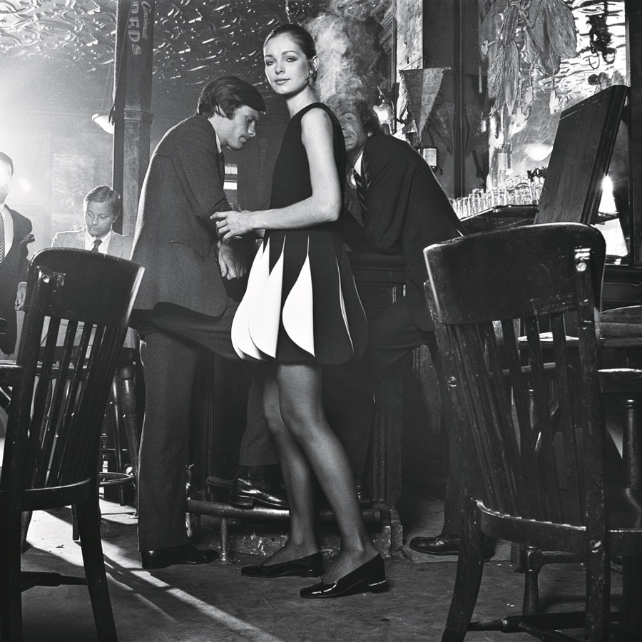 Scène dans un bar montrant une mannequin habillée d'une robe noire et blanche cinétique de Pierre Cardin.